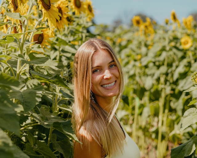 A woman smiling in a field of sunflowers.