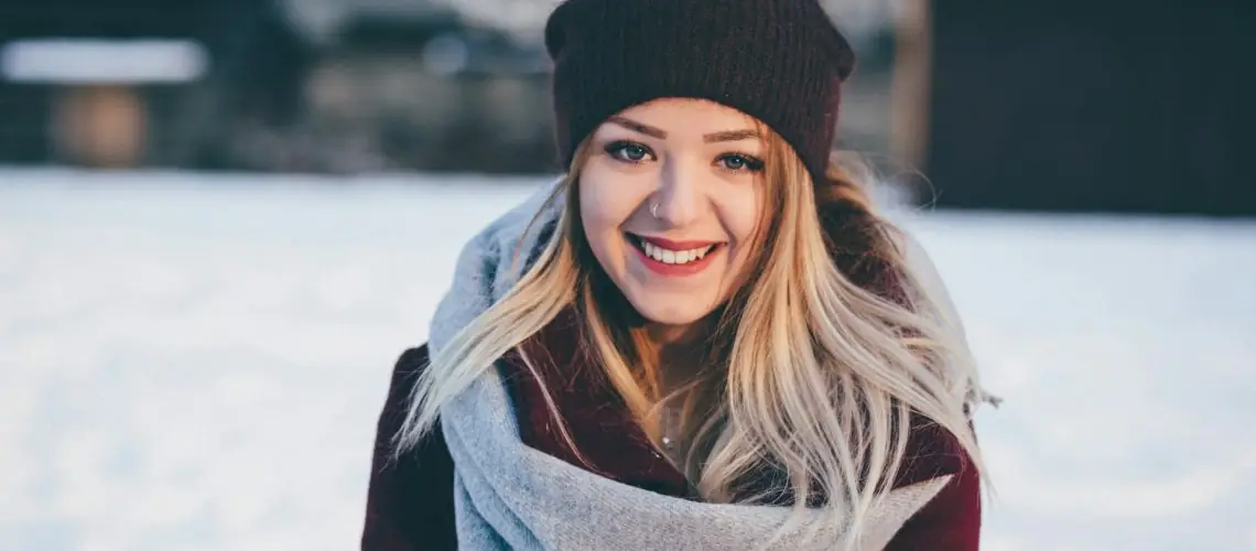 A smiling woman wearing a brown and maroon coat in a field of snow