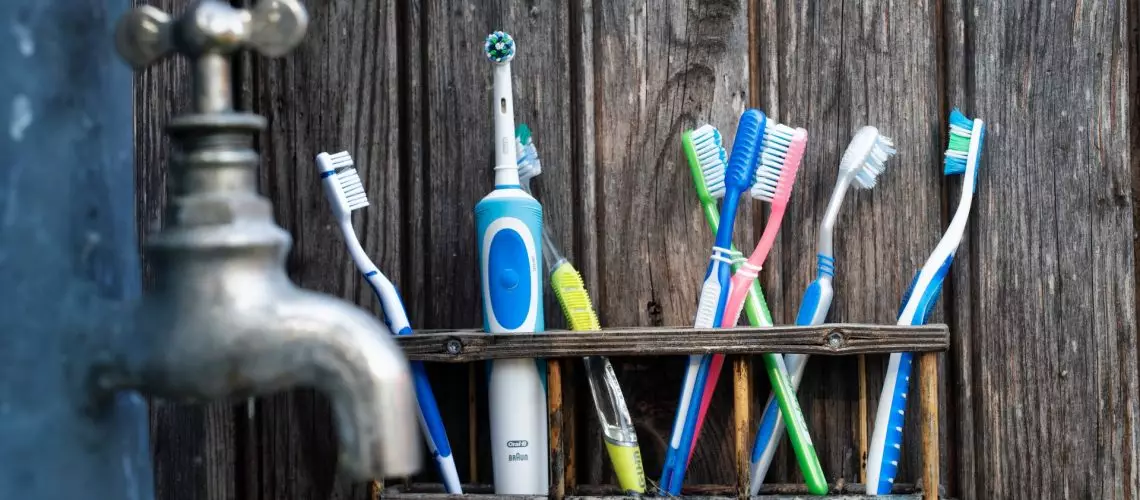 A wooden shelf of toothbrushes in assorted colors by a faucet